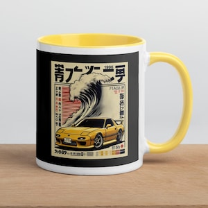 Puede incluir: Taza de cerámica blanca con interior y asa amarillos. La taza presenta un gráfico de un coche deportivo amarillo con una gran ola y texto japonés sobre un fondo negro.