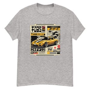 Könnte beinhalten: Hellgraues T-Shirt mit einer Grafik eines gelben Sportwagens mit schwarzen Streifen und japanischem Text. Das Design enthält japanische Schriftzeichen, eine Welle und die Zahl 96. Das Shirt ist ein Freizeitartikel.