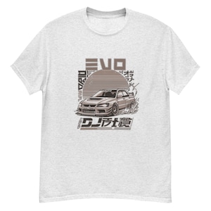 Puede incluir: Una camiseta gris con un gráfico de un Mitsubishi Lancer Evolution blanco con el texto "Evo" y caracteres japoneses. El coche está sobre un fondo de puesta de sol con un sol naciente.