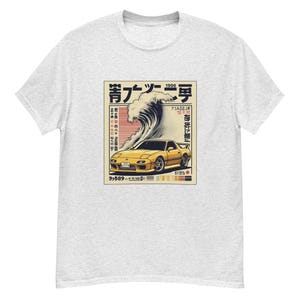 Puede incluir: Camiseta gris claro con un diseño de coche deportivo amarillo, una gran ola y texto japonés. El gráfico tiene una estética vintage con una paleta de colores amarillo, azul y rojo.