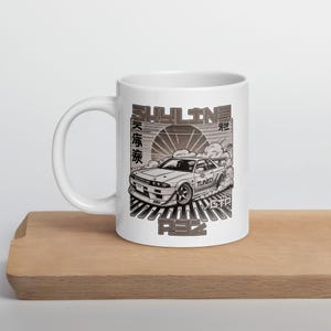 May include: White ceramic mug with a black and white graphic of a sports car, the text "SKYLINE", and Japanese characters. The design includes a rising sun and stylized smoke effects, with the text "R32" at the bottom.