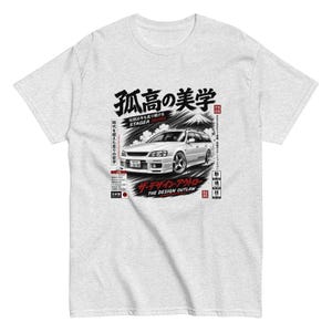 May include: A light gray short-sleeve t-shirt featuring a graphic print of a white station wagon car. The design includes Japanese text, a mountain illustration, and the English text "THE DESIGN OUTLAW" and "STAGEA 260RS" in black and red.