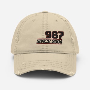 May include: A beige distressed baseball cap with black embroidery that reads "987 SINCE 2004".