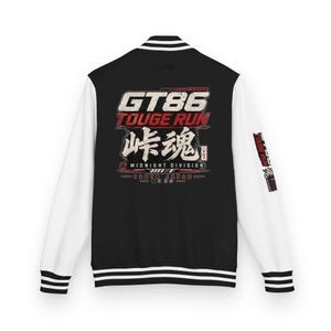 Könnte beinhalten: Eine schwarz-weiße Collegejacke mit einer Grafik auf der Rückseite, die den Text GT86 TOUGE RUN, japanische Schriftzeichen und MIDNIGHT DIVISION zeigt. Der Ärmel trägt ebenfalls den Text TOUGE RUN. Die Jacke hat einen schwarzen Rumpf, weiße Ärmel und gestreifte Bündchen.