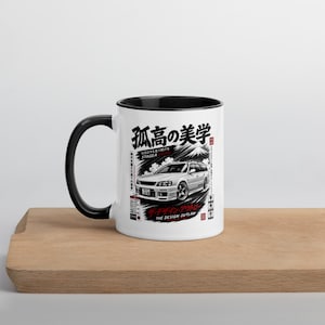 May include: A white ceramic mug with a black handle and interior, featuring a graphic illustration of a white station wagon car, Japanese kanji text, and the English phrase The Design Outlaw printed on the front surface.