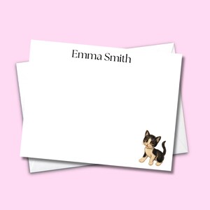 May include: A white rectangular stationery card featuring the black printed name Emma Smith centred at the top and a small, detailed illustration of a black and white kitten positioned in the bottom right corner of the card surface.