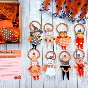 May include: A DIY Halloween ornament kit featuring eight character cutouts with pipe cleaner bodies and gold tinsel halos. The set includes a cardboard box with supplies, orange pipe cleaner carrots with buffalo check bows, and an instruction sheet.