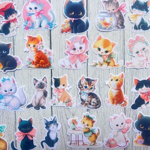 以下が含まれることがあります： 黒、オレンジ、白など、さまざまな色のヴィンテージスタイルの猫のステッカーのコレクション。各ステッカーは、リボンや花のアクセントが付いたものなど、さまざまな猫のデザインを特徴とし、明るい木目調の背景に配置されています。