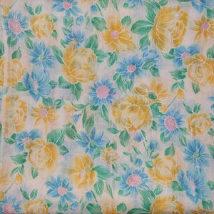 May include: A white fabric with a floral pattern featuring yellow and blue flowers. The fabric has a vintage feel and is perfect for crafting projects.
