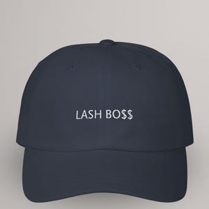 May include: Navy blue baseball cap with the text "LASH BO$$" embroidered in white. The cap has a curved brim and a structured crown. A stylish accessory for anyone in the lash industry.
