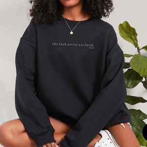 May include: Black sweatshirt with the text "the lash artist uniform" in white lettering.
