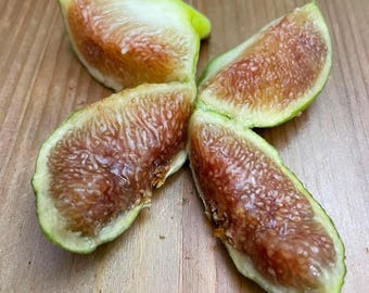 May include: Four fig wedges arranged in a starburst pattern. The figs have a green exterior and a deep reddish-brown interior filled with tiny seeds. The fruit is on a wooden surface.
