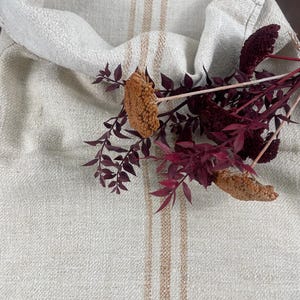 May include: A white linen sack with brown stripes, folded over and decorated with dried burgundy flowers.