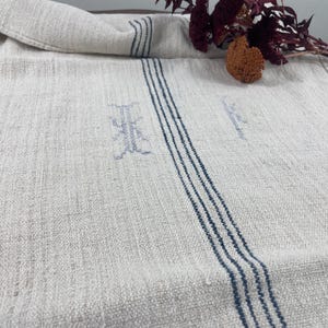 Pode incluir: Um corredor de mesa de linho branco com listras azuis e um desenho bordado azul desbotado.