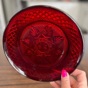 May include: A red glass plate with a diamond pattern and a starburst design in the centre.