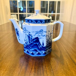 以下が含まれることがあります： 白と青の磁器ティーポット。航海のシーンのデザイン。六角形の形状、湾曲した注ぎ口、ハンドルが特徴です。蓋には小さなノブが付いています。青いデザインは海を航海する船を描いています。
