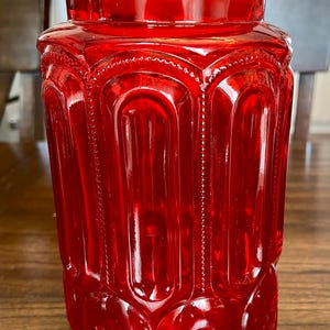 Op de afbeelding: Een rode glazen pot met een getextureerd, reliëfdesign. De pot heeft een ronde, brede opening en een licht uitlopende basis.