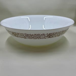 Puede incluir: Un cuenco redondo blanco con un diseño floral marrón alrededor del borde. El cuenco tiene un diseño sencillo y elegante, adecuado para servir ensaladas, pasta u otros platos. Fabricado con un material duradero.