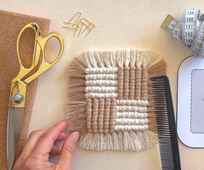 Puede incluir: Un posavasos de macram&eacute; hecho a mano en colores beige y crema. El posavasos cuadrado presenta un dise&ntilde;o tejido con un borde con flecos. Tambi&eacute;n se ven tijeras doradas, clips, un peine y una cinta m&eacute;trica.