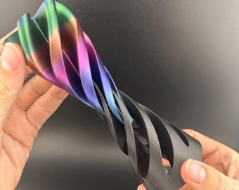 May include: A multi-colored, abstract sculpture with a twisted, spiral design. The top portion transitions from green to purple, while the bottom is black. The object is held against a dark background.
