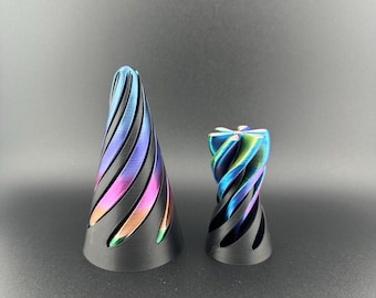 May include: Two decorative objects with a black base and a colorful, iridescent spiral design. The larger object is cone-shaped, while the smaller one is cylindrical. The colors include blue, purple, green, and gold.