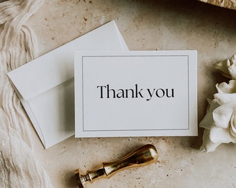 May include: A white card with black text that reads "Thank you". The card is sitting on a light brown surface with a white envelope and a gold wax seal.