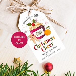 May include: White gift tag with a red and green Christmas theme. It features a jar of jam with a gingerbread man and an orange. The text reads "spreading a little Christmas Cheer one jar at a time!" and "THE FERNANDEZ FAMILY".