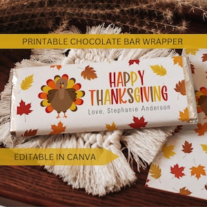 May include: A white chocolate bar wrapper with a Thanksgiving theme. The wrapper features a cartoon turkey, autumn leaves, and the words "Happy Thanksgiving." The text "Love, Stephanie Anderson" is also included.