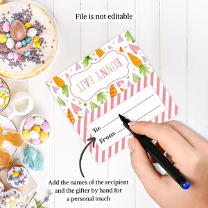 Puede incluir: Etiqueta de regalo rosa y blanca con tem&aacute;tica de conejito con un patr&oacute;n a rayas y un espacio para escribir "Para:" y "De:". La etiqueta tiene un conejito de dibujos animados y zanahorias. El texto "Bunny Bail" est&aacute; escrito en la etiqueta.