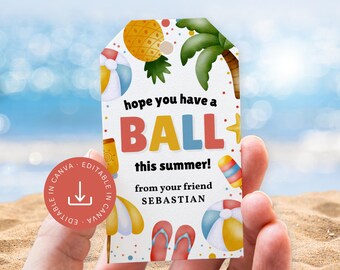 May include: A summer-themed gift tag with a beach ball, palm tree, and pineapple illustration. The tag reads "hope you have a BALL this summer!" and includes the name "SEBASTIAN". The tag is held in a hand.