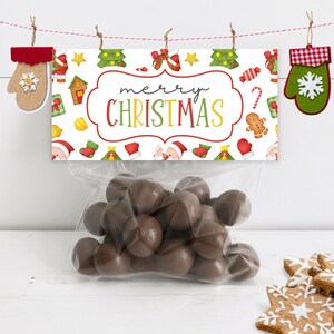 May include: A white gift bag with a red and green Christmas themed tag that says "merry CHRISTMAS". The tag has a variety of Christmas icons including a gingerbread man, candy canes, and Christmas trees. The bag is filled with chocolate candies.