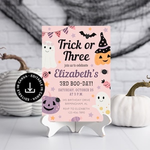 May include: A pink Halloween invitation with the text "Trick or Three" and "Elizabeth's 3rd Boo-Day!" features illustrations of ghosts, pumpkins, and bats. The invitation is displayed on a white stand with pumpkins in the background.