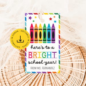 May include: A rectangular gift tag with a rainbow striped border featuring six colorful crayons and small stars at the top. The text reads: here's to a BRIGHT school year! FROM MS. FERNANDEZ. A yellow circular badge with a download icon is attached.