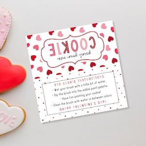 Puede incluir: Una tarjeta blanca con corazones rojos y rosas impresos en ella. La tarjeta tiene instrucciones para una actividad de "Pinta tu propia galleta". El texto dice "Instrucciones para la galleta de pintar: Moja tu pincel con un poco de agua. Sumerge el pincel en la paleta de pintura comestible. &iexcl;Divi&eacute;rtete pintando tu galleta! Limpia el pincel con agua entre colores. &iexcl;Feliz D&iacute;a de San Valent&iacute;n!"
