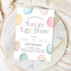 以下が含まれることがあります： カラフルなイースターエッグと「Hop on over for an Easter Egg Hunt」というテキストが書かれた白い招待状。イベントの日時、住所、RSVP情報も記載されています。
