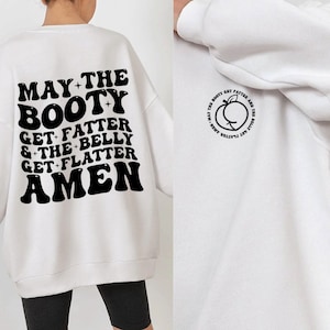 May include: White sweatshirt with a black graphic print on the back that reads "MAY-THE BOOTY GET FATTER & THE BELLY GET FLATTER AMEN". The front of the sweatshirt has a smaller black graphic print of a peach with the text "AMEN-MAY THE BOOTY GET FATTER AND THE BELLY GET FLATTER".