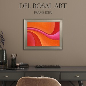 May include: A framed abstract painting featuring flowing, curved bands of color in shades of orange, red, and pink. The artwork is displayed in a metallic silver frame. Above the frame, the text reads DEL ROSAL ART FRAME IDEA.