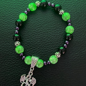 May include: A green and black beaded bracelet with a silver dragon charm. The beads are faceted and have a sparkly finish.