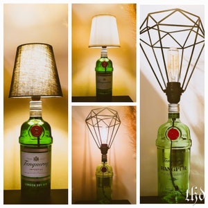 May include: Three different lamps made from repurposed liquor bottles. The lamps are all green glass and have a black metal shade. The first lamp has a white fabric shade, the second lamp has a black metal diamond-shaped shade, and the third lamp has a black metal cage shade. The bottles all have labels that say "Tanqueray" and "Rangpur".