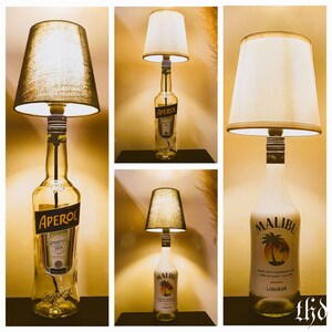 May include: Three table lamps made from liquor bottles with fabric lampshades. The bottles are clear glass with labels. The lamps are lit and the shades are white. The bottles are labeled Aperol and Malibu.