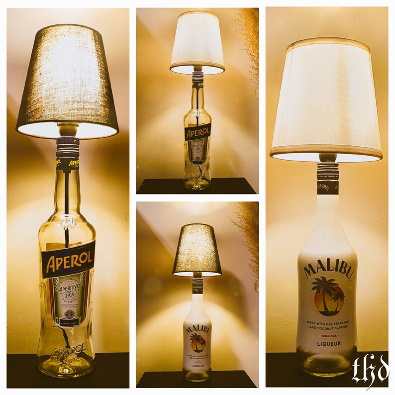 May include: Three table lamps made from liquor bottles with fabric lampshades. The bottles are clear glass with labels. The lamps are lit and the shades are white. The bottles are labeled Aperol and Malibu.