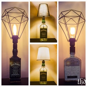 May include: Three table lamps made from repurposed Jack Daniel's bottles. The lamps have different shades and bases. One lamp has a black wire cage shade, another has a white fabric shade, and the third has a black fabric shade. The bottles are labeled "Jack Daniel's Tennessee Apple" and "Gentleman Jack".
