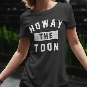 Op de afbeelding: Zwart T-shirt met witte tekst die "Howay the Toon" zegt.