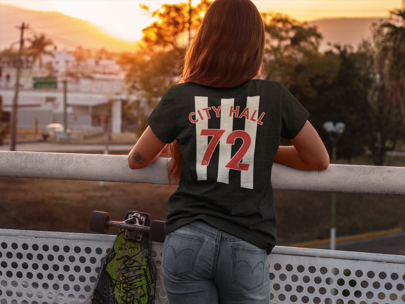 K&ouml;nnte beinhalten: Schwarzes T-Shirt mit wei&szlig;en Streifen und rotem Text, der "City Hall 72" lautet.