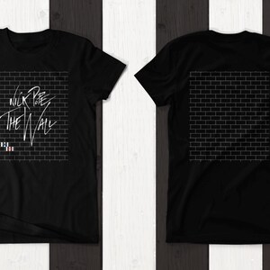 Pode incluir: Camiseta preta com um gr&aacute;fico branco de uma parede de tijolos e o texto "Nick Lowe The Wall". A parte de tr&aacute;s da camiseta apresenta um gr&aacute;fico branco de uma parede de tijolos.