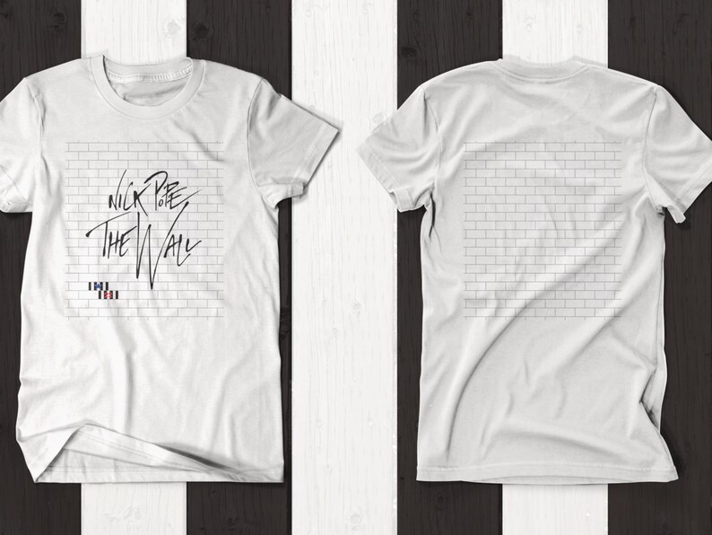 Pode incluir: Camiseta branca com uma imagem em preto e branco de uma parede de tijolos e o texto "Nick Lowe The Wall" na frente. A parte de tr&aacute;s da camiseta apresenta um design de parede de tijolos.