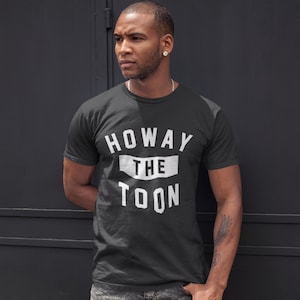 Op de afbeelding: Een zwart T-shirt met witte tekst die "Howay the Toon" zegt.