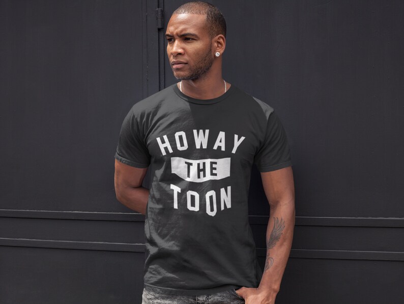 Op de afbeelding: Een zwart T-shirt met witte tekst die "Howay the Toon" zegt.