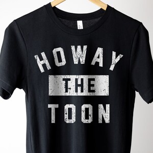 May include: Black t-shirt with white text that reads "Howay the Toon" in a distressed font.