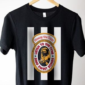 K&ouml;nnte beinhalten: Schwarzes T-Shirt mit einem wei&szlig;en Streifenmuster. Ein gelber Kreis mit rotem und wei&szlig;em Text lautet "Howay the Toon City Hall Newcastle Upon Tyne, Tuesday, 13th April, 1972, 7:30 PM Listen to the Tyne Sing Sweet Songs Playing with the Mads"